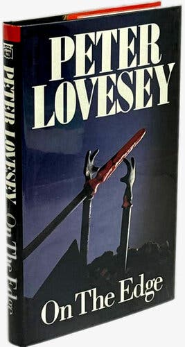 A dark blue cover with a design at the center featuring two metal hands and a spear drenched in red. Above, in thick white lettering, are the words “Peter Lovesey,” and underneath, “On the Edge.”